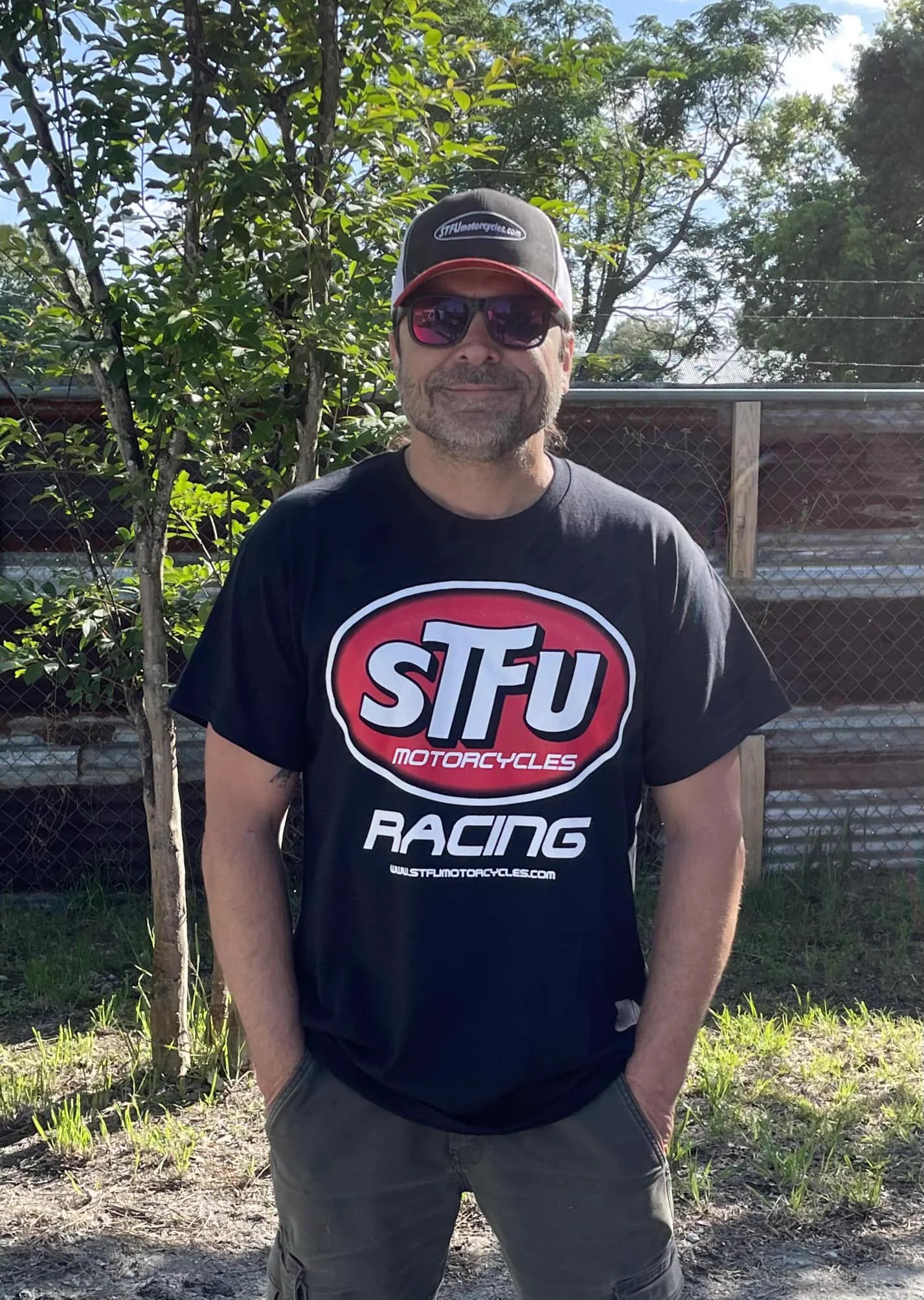 Scott smiling outdoors in an STFU Motorcycles Racing shirt and cap