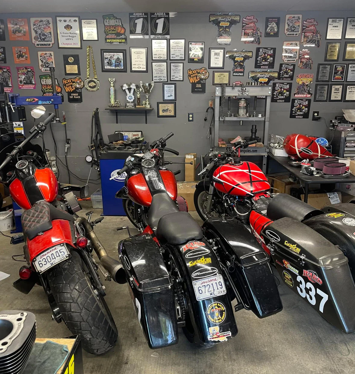 Dragbob, Dragbag, and Eddie parked together in Scott's workshop beneath a wall covered with race trophies and winner plaques