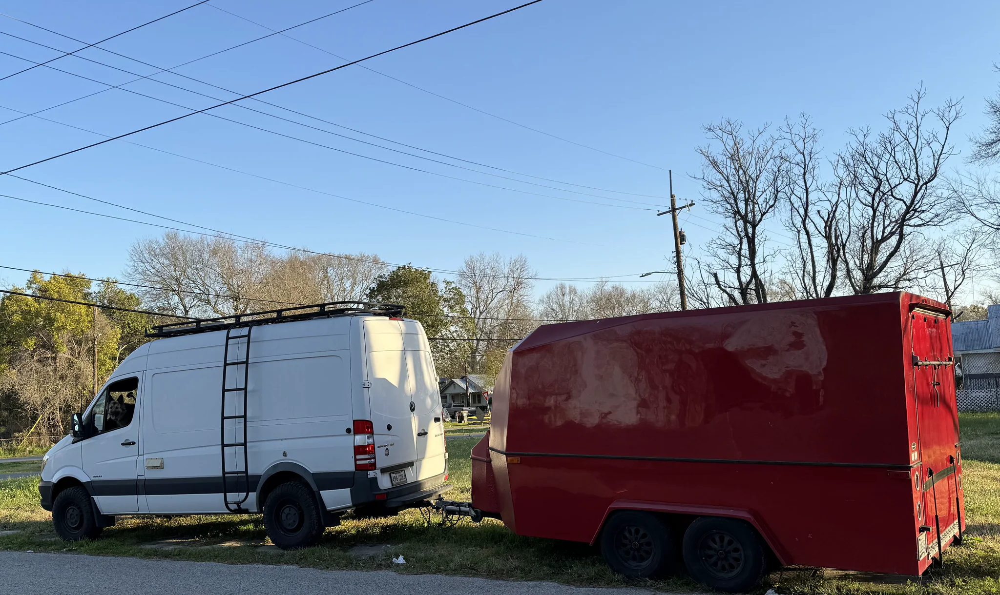 Two white Mercedes Sprinter vans beside Scott's red enclosed race trailer on a residential street